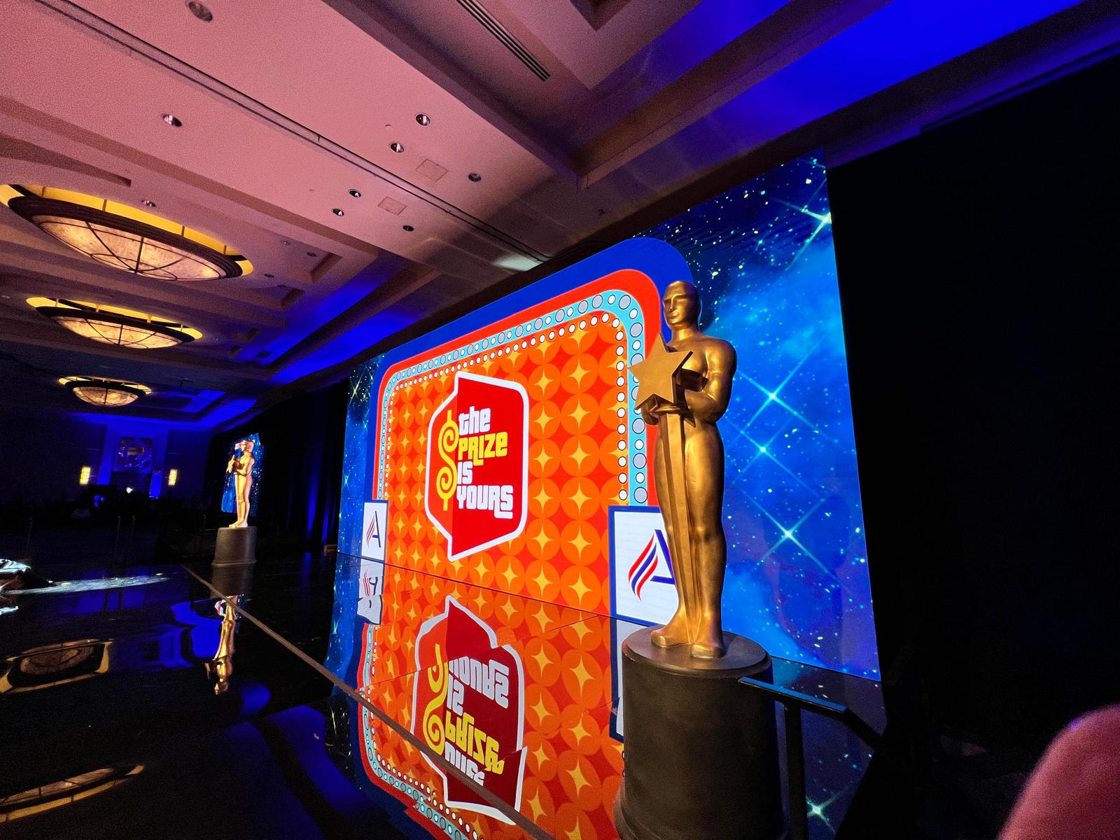 Gold award statue on the reflective acrylic show floor beside the LED wall at Adventist HealthCare's Employee Gala