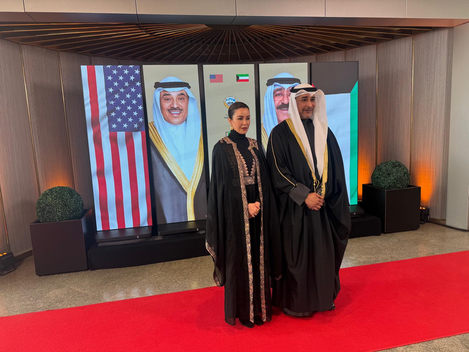 Guests in traditional dress on the red carpet in front of LED poster displays at a Kuwait Banking Association reception